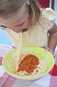 Small girl eating spaghetti with tomato sauce