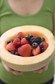 Woman holding fresh berries in hollowed-out cantaloupe melon