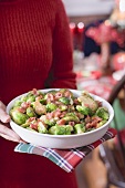 Woman holding dish of Brussels sprouts with bacon (Christmas)