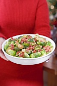 Woman holding dish of Brussels sprouts with bacon