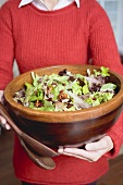 Frau hält grosse Schüssel Blattsalat mit Nüssen