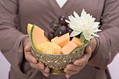 Woman holding bowl of fresh fruit with water lily