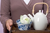 Woman holding tray of tea things (teapot, tea bowl, flower)