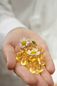 Hand holding vitamin capsules and chamomile flowers