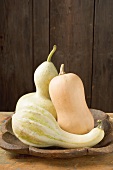 Three squashes in bowl in front of wooden wall