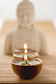Three tea lights on bamboo mat in front of Buddha statue