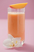 Glass of mango smoothie with wedge of mango and orchid
