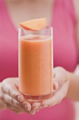 Woman holding glass of mango smoothie with wedge of mango