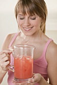 Woman holding jug of fruit juice with ice cubes