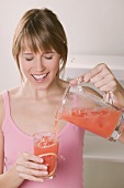 Woman pouring pink grapefruit juice into glass