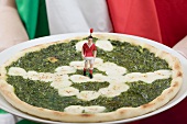 Fussballfan hält Spinatpizza mit Mozzarella (Italien)