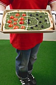 Female footballer holding spinach pizza with tomatoes & olives