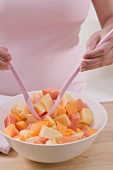Woman taking fruit salad out of bowl with salad servers