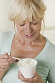 Frau isst Joghurt aus Plastikbecher