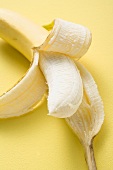 Banana, half peeled, on yellow background