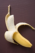 Banane, halb geschält, auf braunem Untergrund