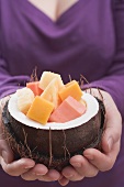 Frau hält ausgehöhlte Kokosnuss mit exotischem Fruchtsalat