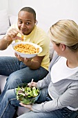 Couple on sofa with peanut puffs and salad
