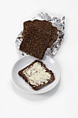 Slices of black bread in foil, a slice buttered on plate