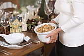 Woman placing dish of bread stuffing on Christmas table