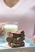 Woman holding brownies and glass of milk on square plate