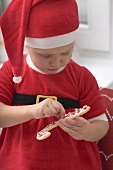 Kleines Mädchen im Weihnachtsmannkostüm verziert Plätzchen