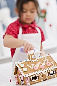 Small girl decorating gingerbread house with sugar
