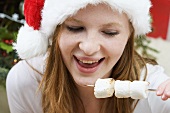 Woman in Father Christmas hat eating marshmallows on stick