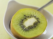 Half a kiwi fruit in bowl with spoon