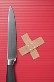 Knife and crossed sticking plasters on red background