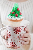 Frau hält Cupcake auf grosser Tasse zu Weihnachten