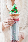 Frau hält Cupcake auf Thermobecher zu Weihnachten