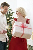 Woman holding large Christmas parcel, man holding glass of wine