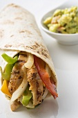 Wrap filled with chicken and peppers, guacamole beside it
