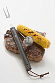 Beef steak with corn on the cob, carving fork & thermometer