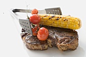 Grilled T-bone steak, corn on the cob, tomatoes, grill tongs