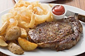 Rib-eye steak with onion rings, ketchup and potato wedges
