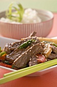 Beef with vegetables & sesame seeds, rice in background (Asia)