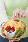 Woman holding basket of nachos with salsa and chilli