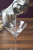 Martini aus Cocktailshaker in Glas gießen