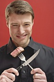 Man holding crossed cutlery with piece of beef steak on fork