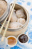 Dim sum in bamboo steamer, two sauces beside it (Asia)