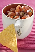Tomato salsa in pot with spoon, nacho beside it (Mexico)