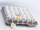 Fresh eggs in an egg tray, one broken