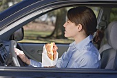 Young woman eating croissant in car
