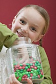 Small girl eating chocolate beans out of sweet jar