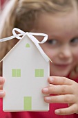 Kleines Mädchen hält Papierhaus (Weihnachtsgeschenk)