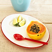 Half a papaya and lemon wedges on plate with spoon