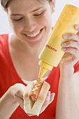 Young woman putting mustard on hot dog