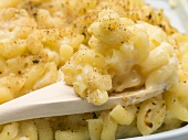 Macaroni cheese in baking dish with wooden spoon (close-up)